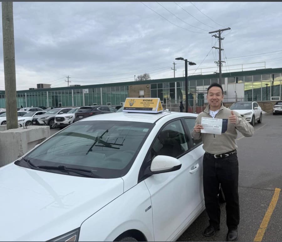 A Rydbie student giving a thumbs up beside a Rydbie car, holding their pass slip