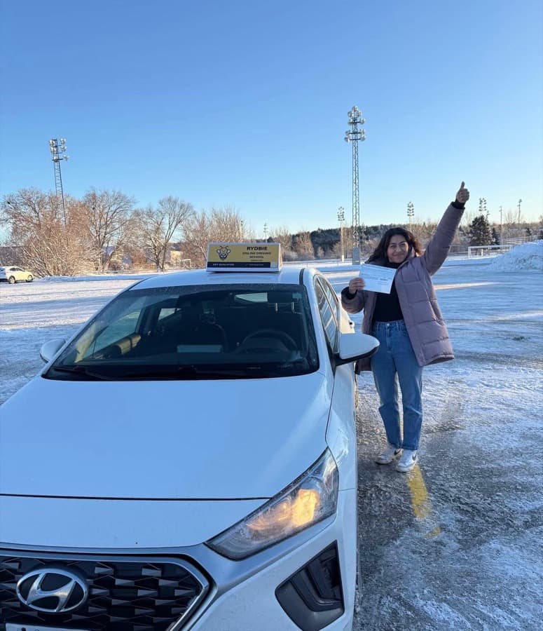 A Rydbie student giving a thumbs up in the snow beside a Rydbie car