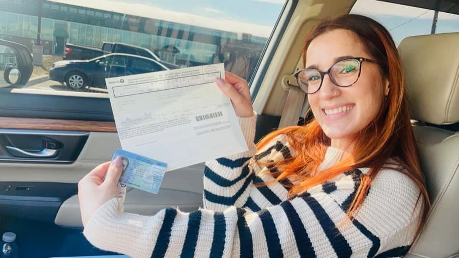A Rydbie student in the car holding up her new Ontario licence card and permit